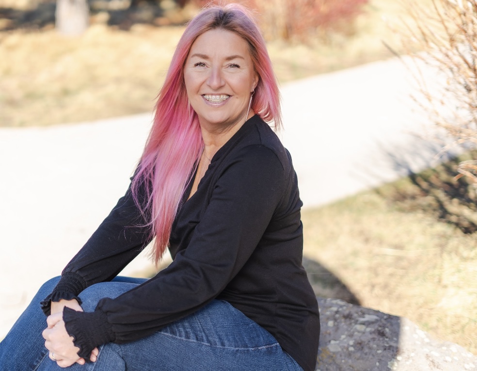 Portrait photo of Michelle Mejaski with long pink hair, smiling outside.